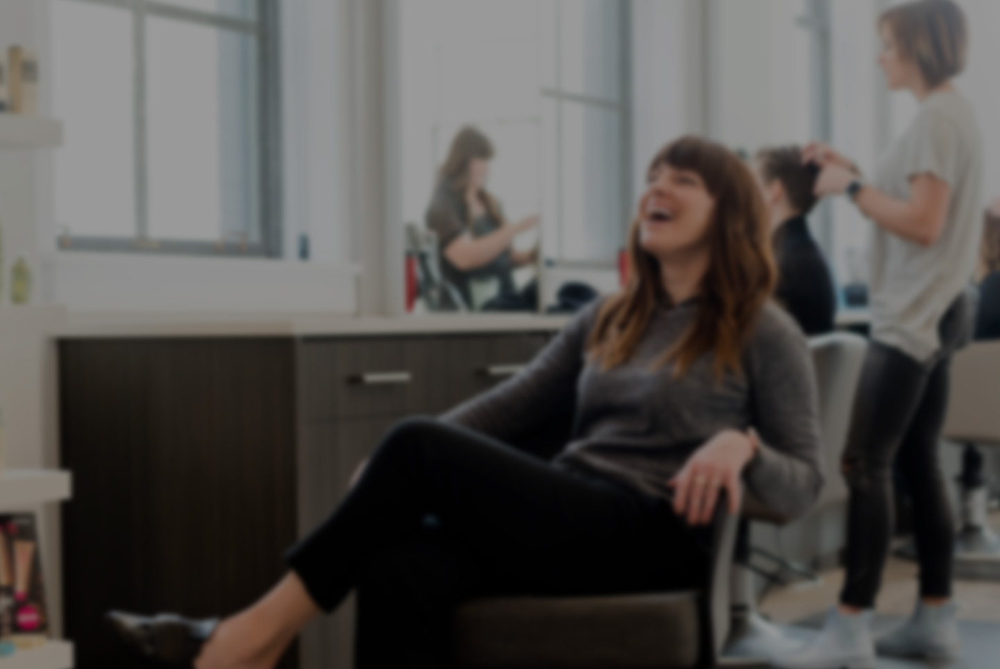 Client laughing in a salon chair while stylists work in the background