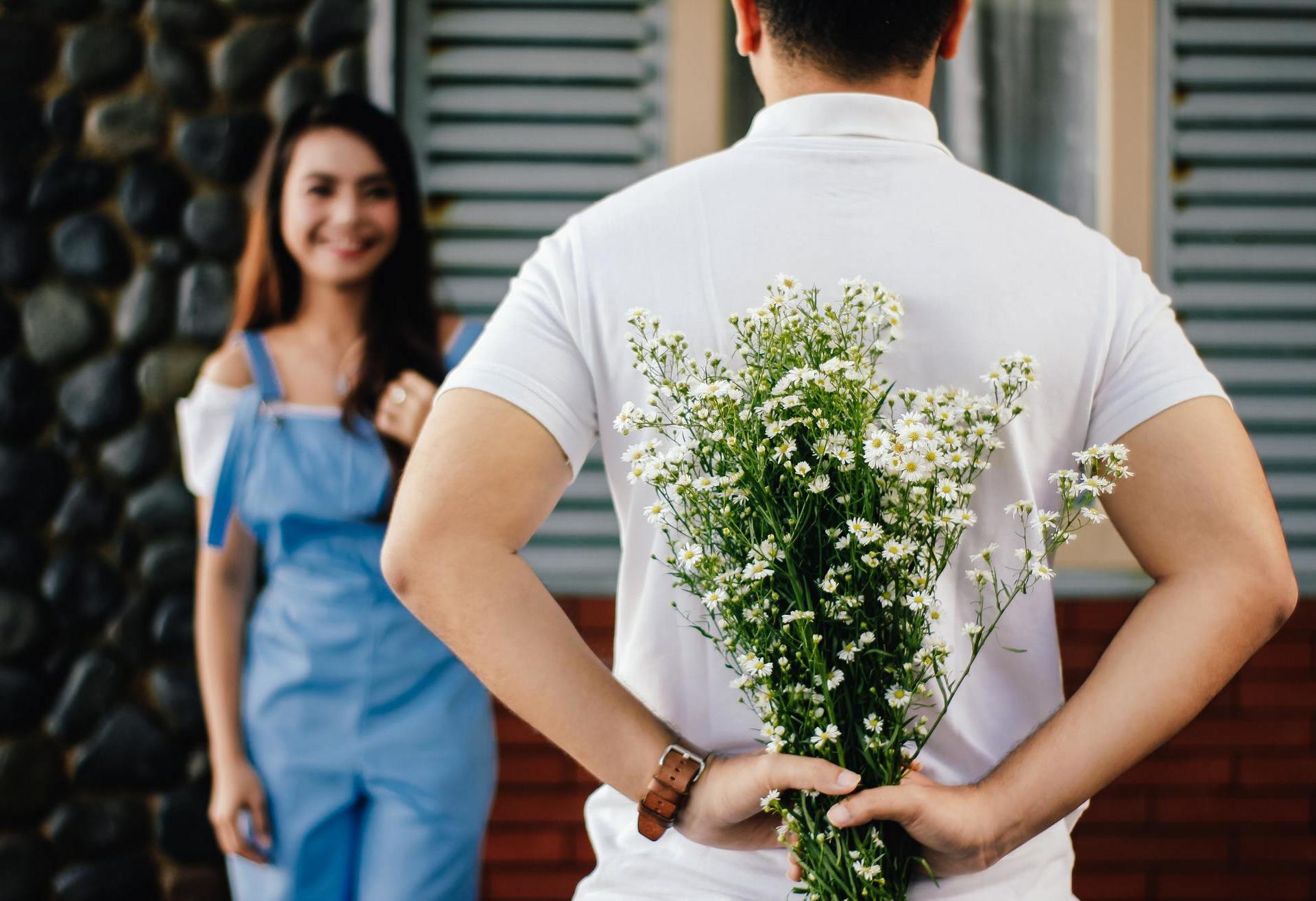 Man holding beautiful flowers behind his back, about to surprise a girl.
