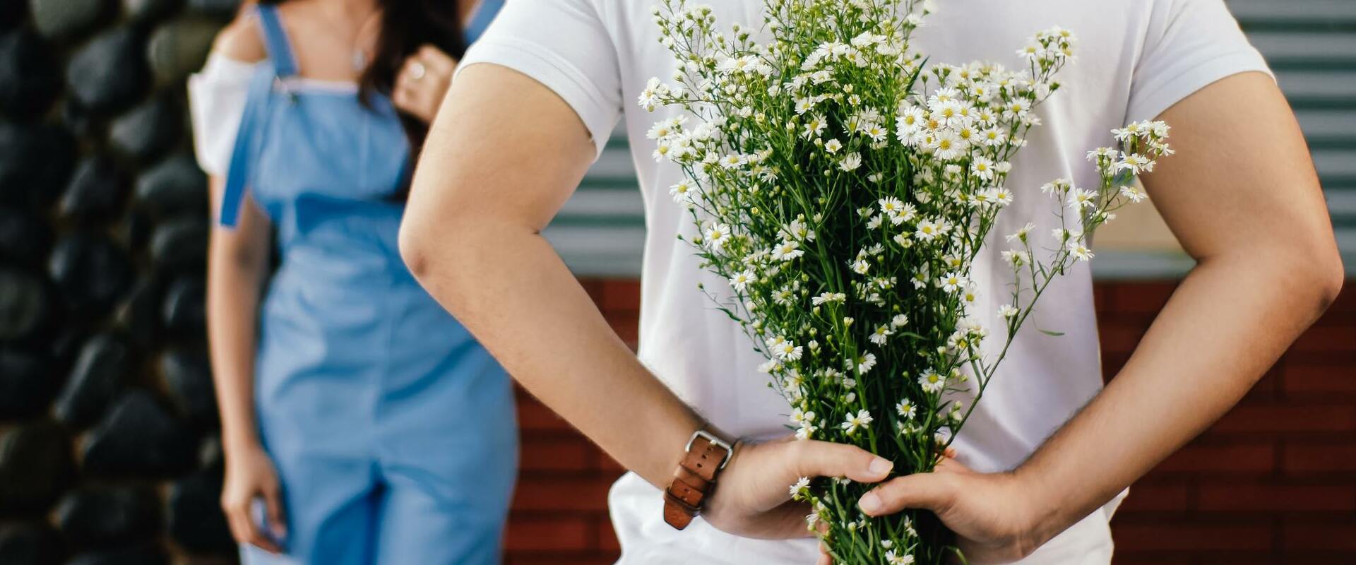 Man holding beautiful flowers behind his back, about to surprise a girl.